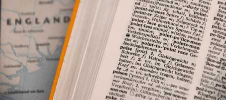 A picture of a dictionary in the word starting with P section, with Poise and Poison visible. Behind it is a map of England.